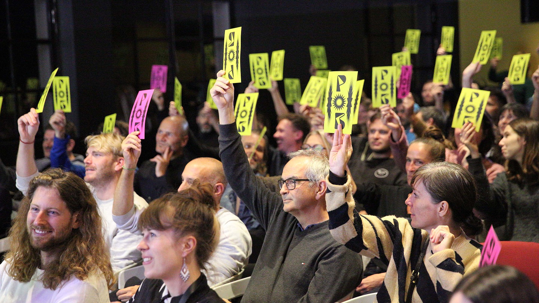 Das Publikum hält seine gelben und pinkfarbenen Stimmzettel hoch. Mit dabei ist auch Peter Stämpfli, Inhaber von Stämpfli Kommunikation.
