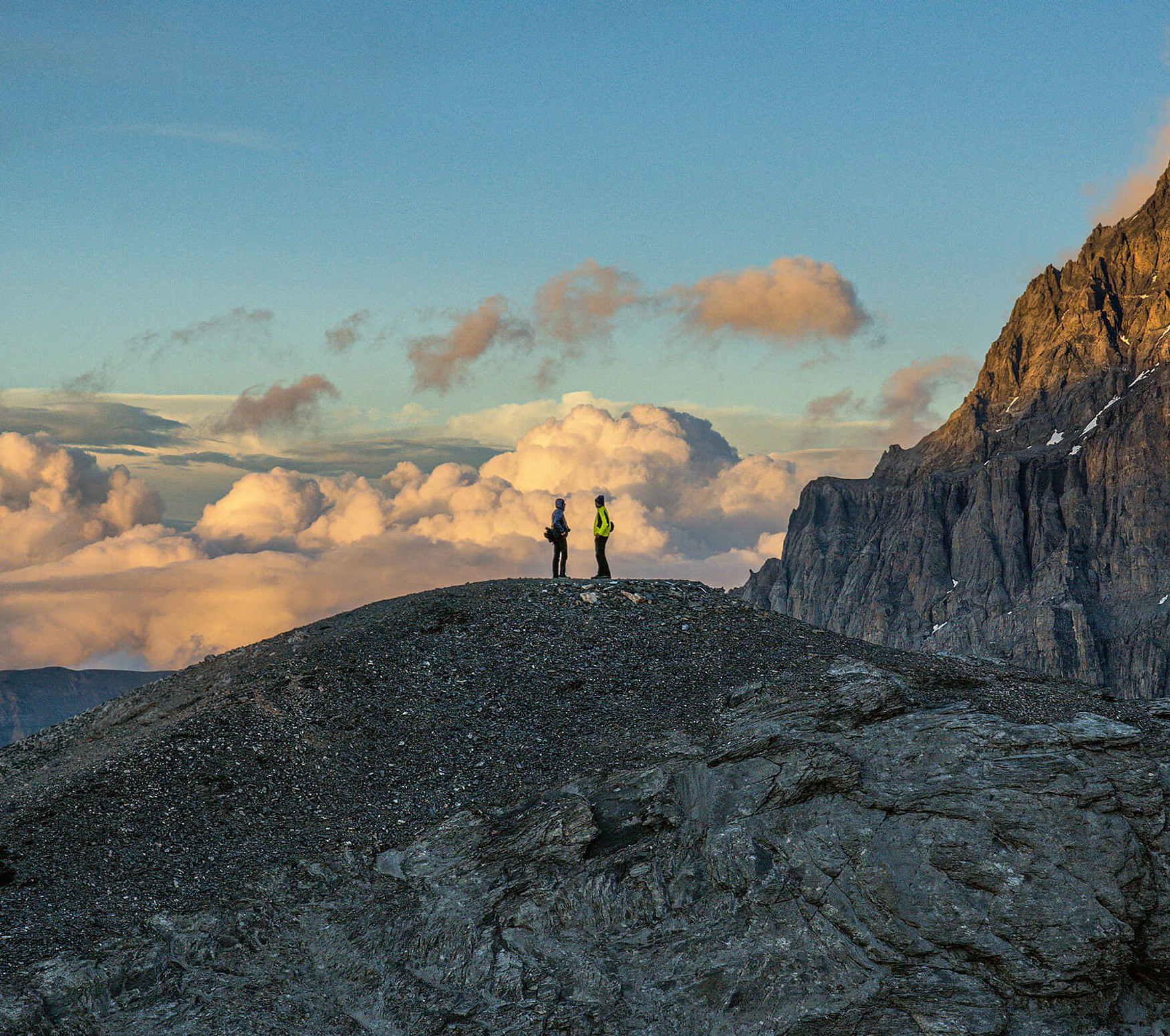 Zwei einsame Wanderer stehen auf einem Gipfel und geniessen die schöne Stimmung.