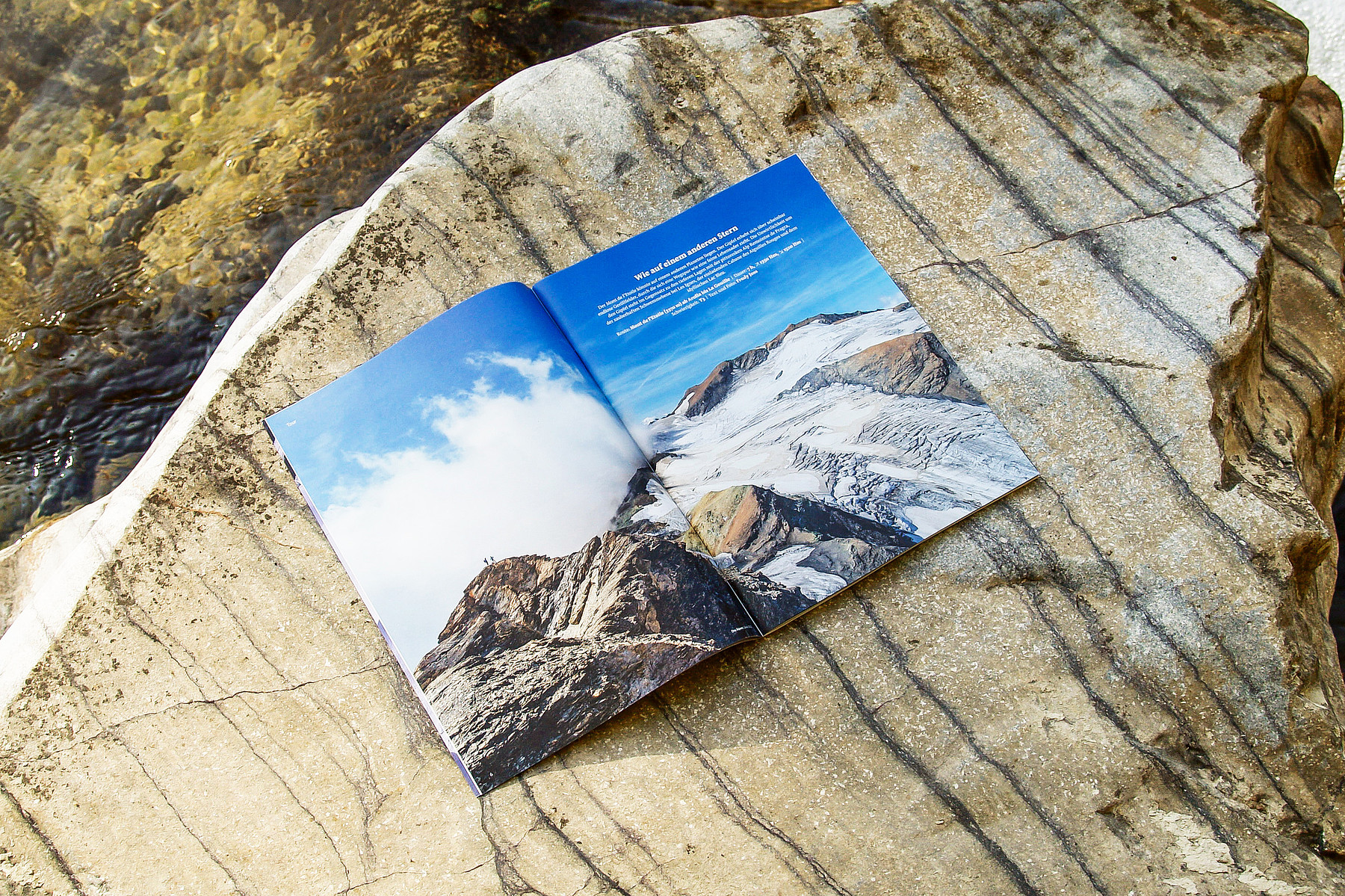 Eine aufgeschlagene Ausgabe der SAC-Zeitschrift «Die Alpen» auf einem Felsbrocken im Grünen: Sie zeigt ein doppelseitiges Schwarz-Weiss-Foto einer Felslandschaft.